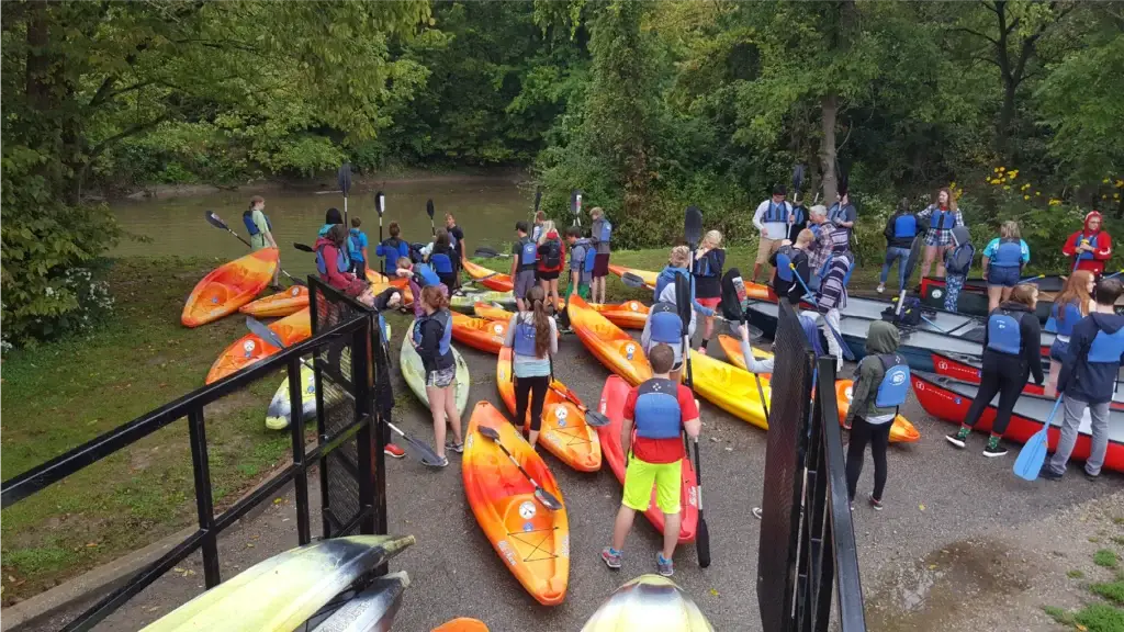 Large group preparing for a kayak adventure with colorful rental kayaks at the Little Miami River launch.