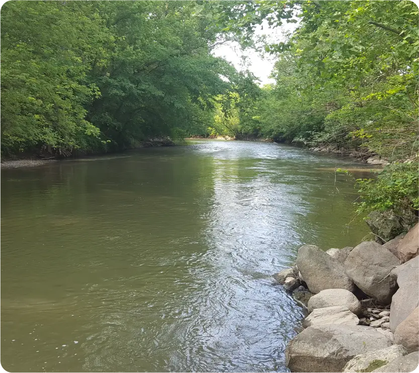 Peaceful view of the Little Miami River flowing through a wooded landscape with rocky shoreline.